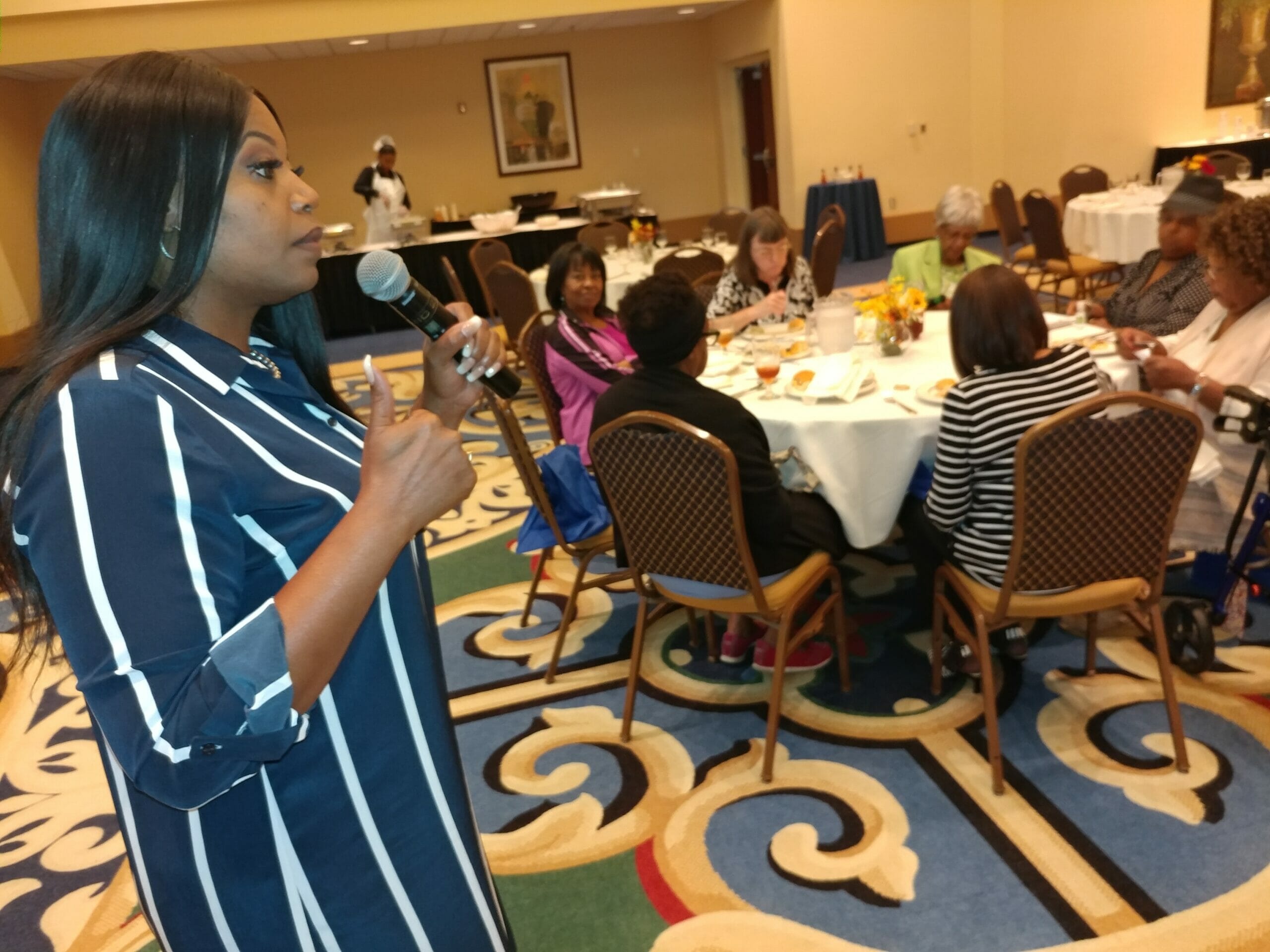 A woman speaking to other adults at an event in a banquet hall.