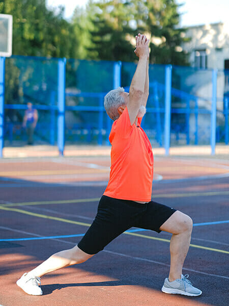 A man in an orange shirt stretching on the tennis court.